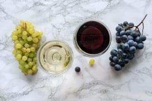 a glass of white wine next to some wine grapes and a glass of red wine next to a bunch of red grapes